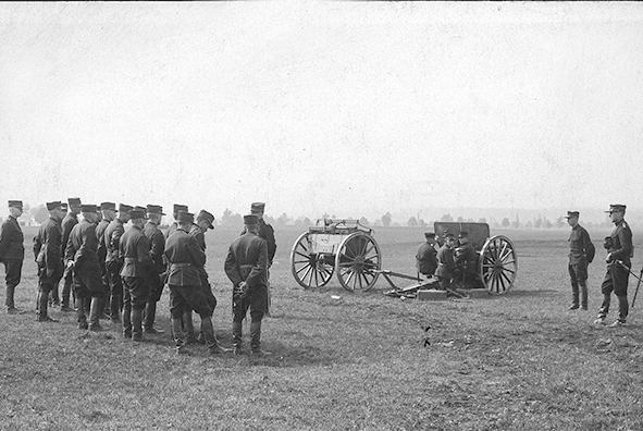 » Un groupe de soldats observe un exercice d'artillerie sur la place d'armes de Thoune, ordonné par deux officiers qui supervisent les opérations.